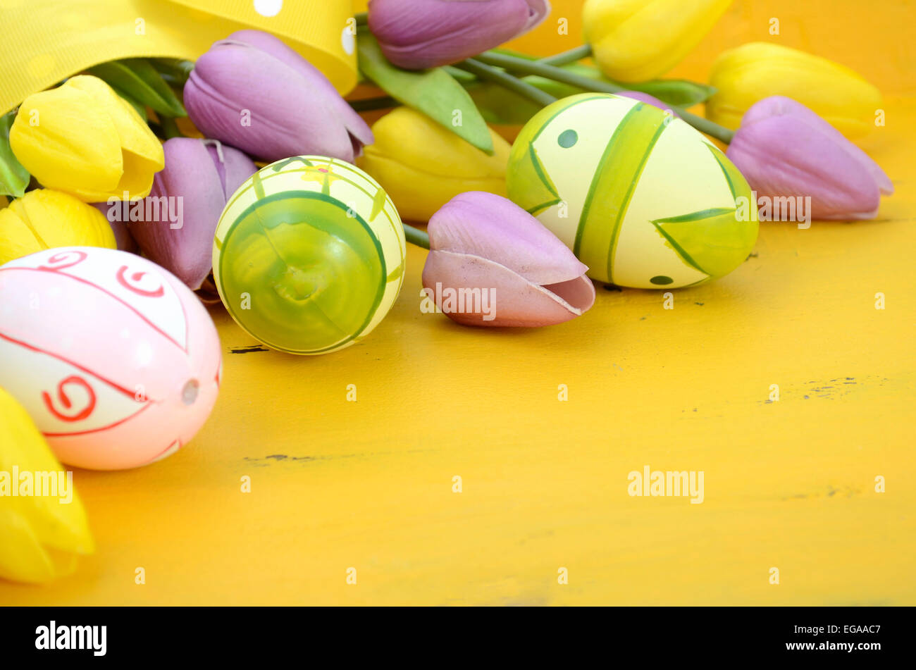 Felice Pasqua sfondo dipinto con le uova di Pasqua, giallo e viola i tulipani di seta e polka dot nastro su stile vintage rustico dis Foto Stock