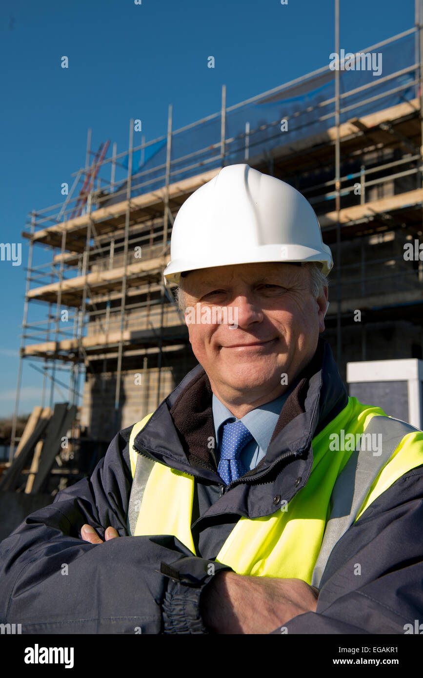 Sorridente ingegnere civile, in piedi di fronte a un sito di costruzione con le braccia piegate. Foto Stock