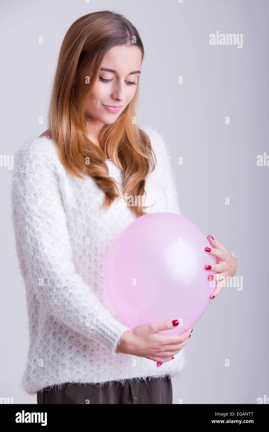 Donna che mantiene un palloncino rosa al suo ventre. Concetto di gravidanza. Foto Stock