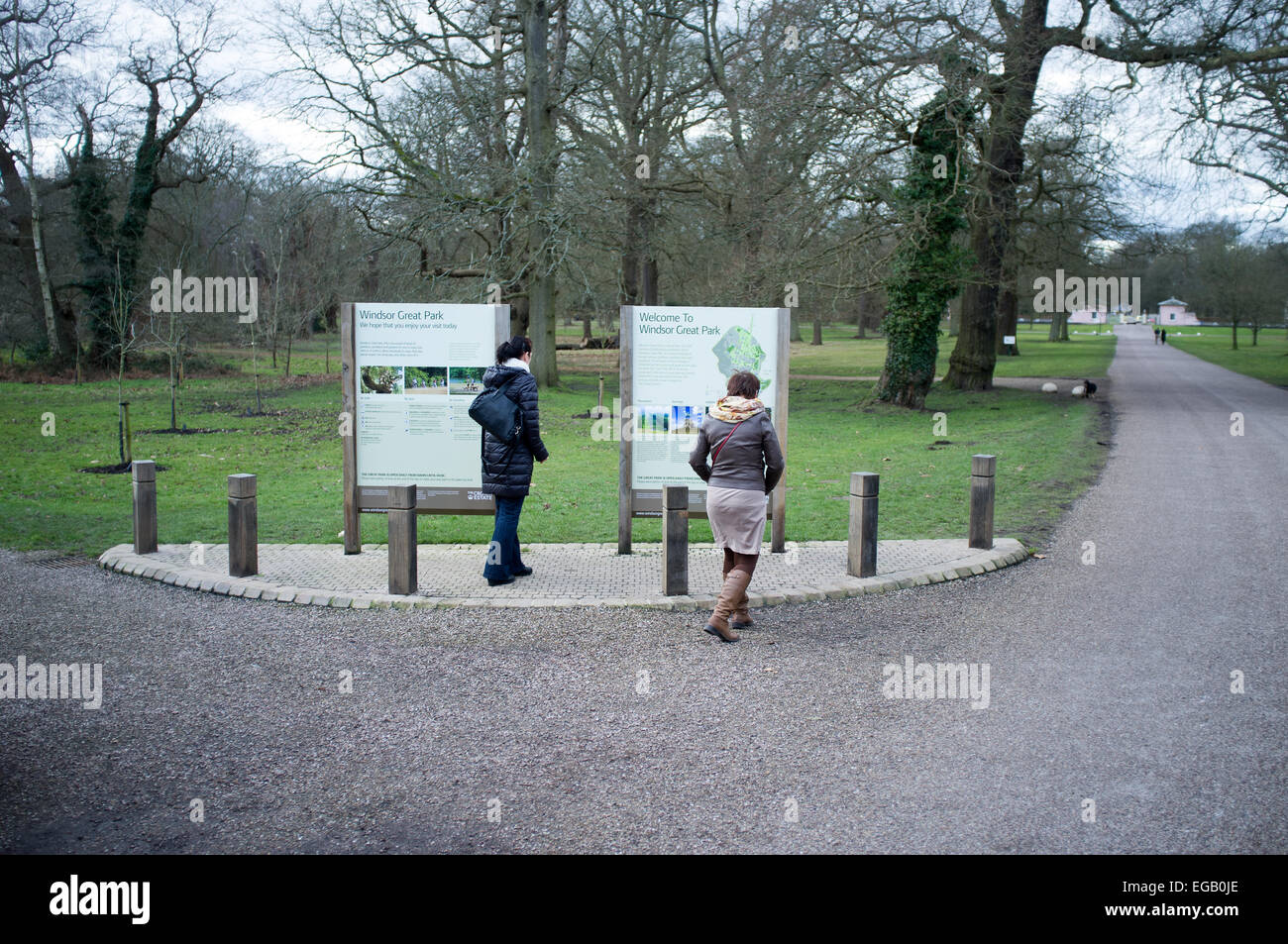 I visitatori a piedi passato un segno informazioni in Windsor Great Park. Le porte della Royal Lodge può essere visto in lontananza. Foto Stock