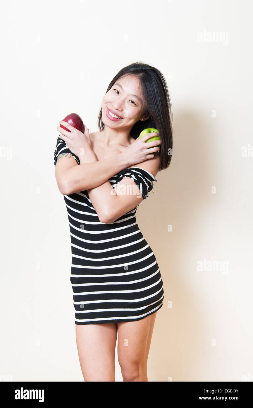 Felice e sorridente giovane bella donna asiatica con due mele rosse e verdi su sfondo bianco Foto Stock