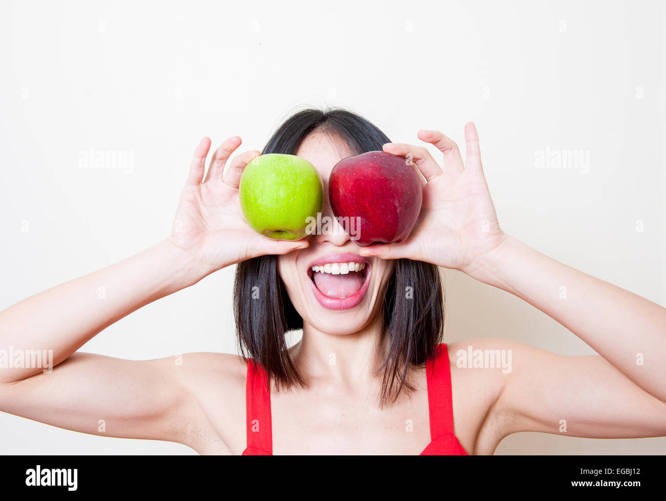 Funny giovane donna ritratto mettendo due mele rosse e verdi sui suoi occhi su sfondo bianco Foto Stock