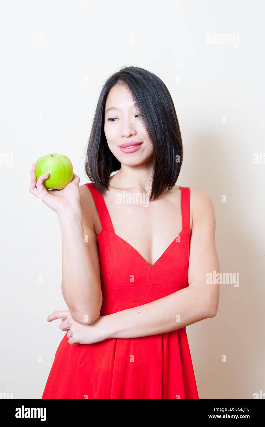 Giovane bella donna asiatica abito rosso in cerca della mela verde sulla sua mano su sfondo bianco Foto Stock