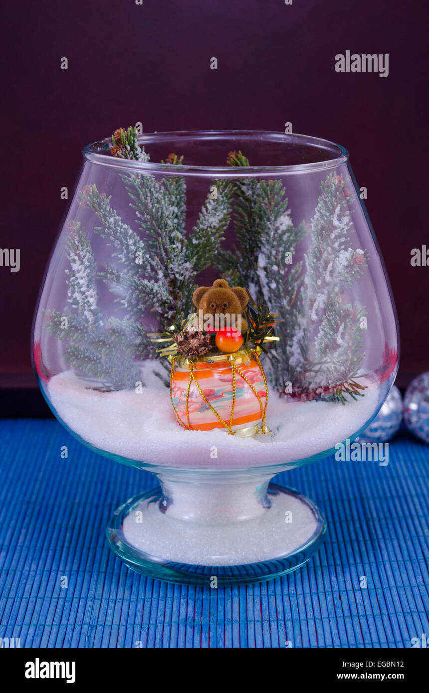 Toy bear suonando la batteria in un vaso di vetro coperti di neve su una tovaglia blu Foto Stock
