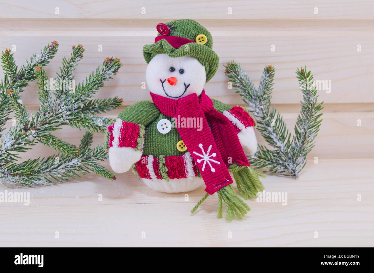 Carino pupazzo di neve indossando un cappello su una superficie in legno circondato con rami di abete cowered con neve, Foto Stock