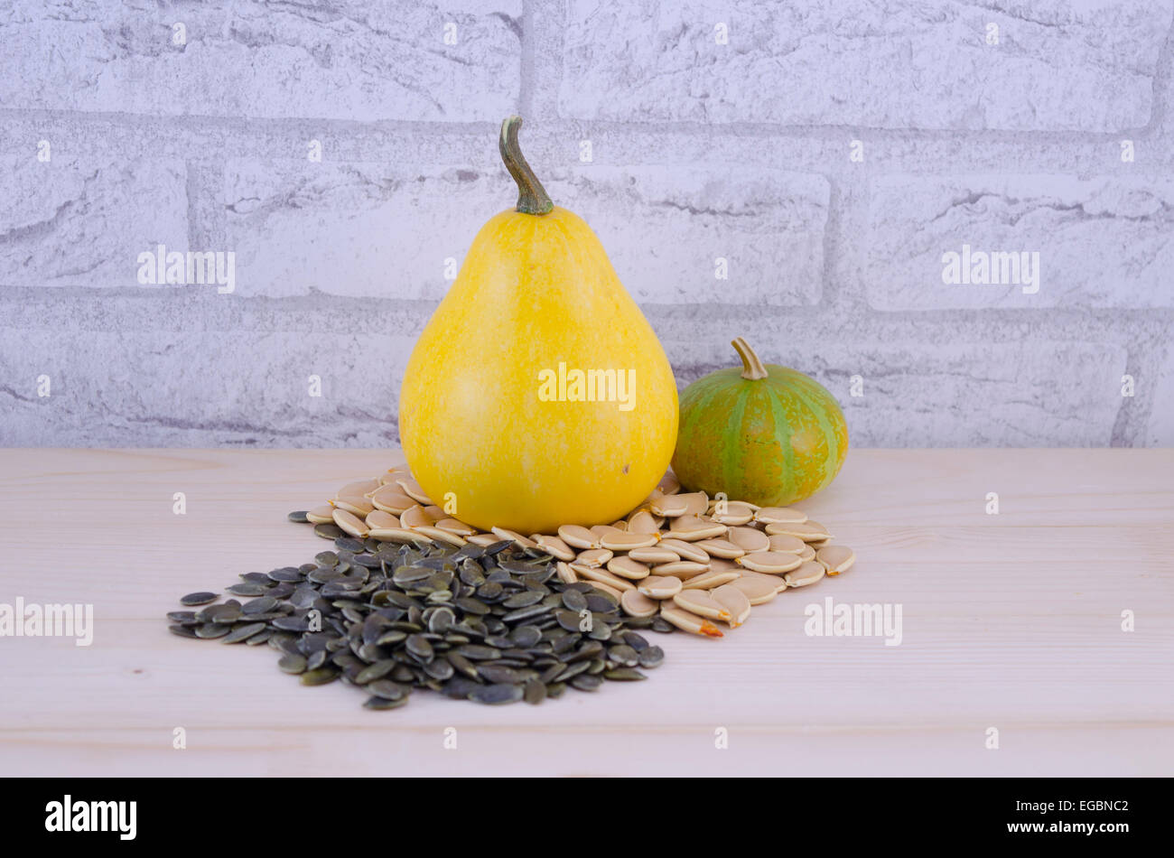Colorato zucche decorative e i semi di zucca su di un tavolo di legno con un muro di mattoni in background Foto Stock