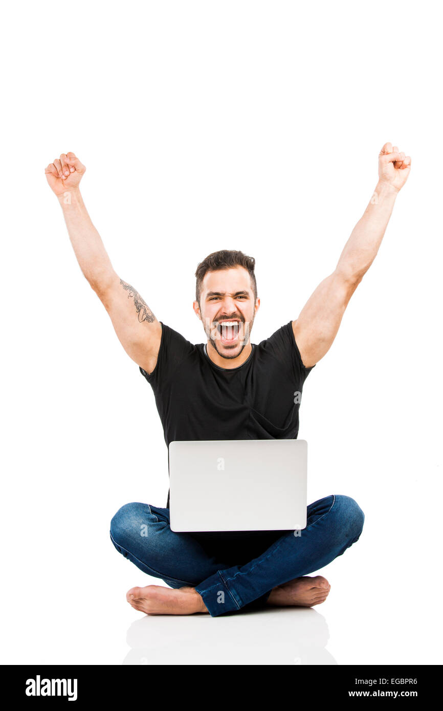 Latino uomo seduto sul pavimento e lavorare con un computer portatile con entrambe le braccia in alto Foto Stock