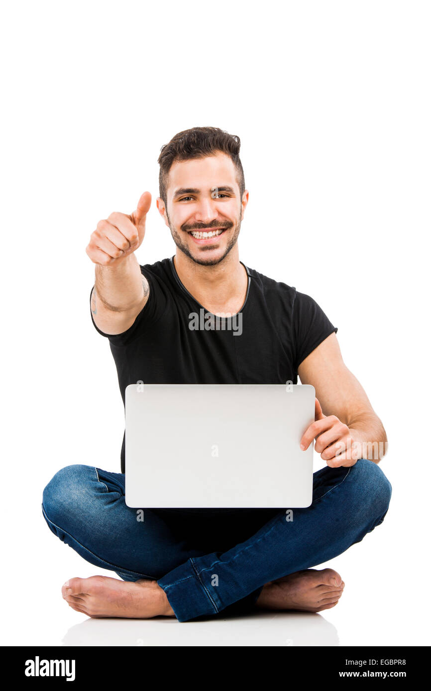 Latino uomo seduto sul pavimento e lavorare con un computer portatile con il pollice in alto Foto Stock