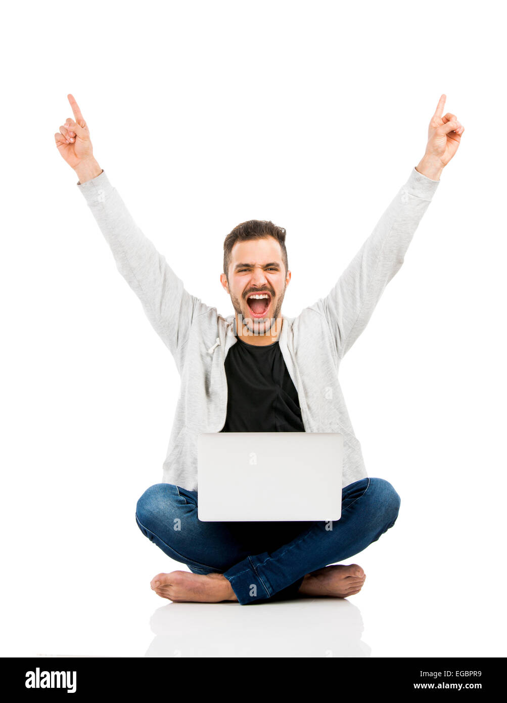 Latino uomo seduto sul pavimento e lavorare con un computer portatile con entrambe le braccia in alto Foto Stock