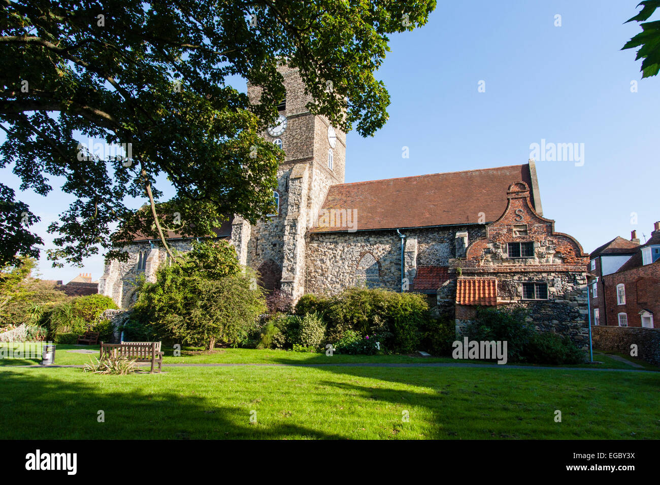 St Peters Norman chiesa, 11 ° secolo edificio in pietra con torre dell'orologio centrale contro il cielo blu chiaro presso la storica città mercato di Sandwich, Kent. Foto Stock