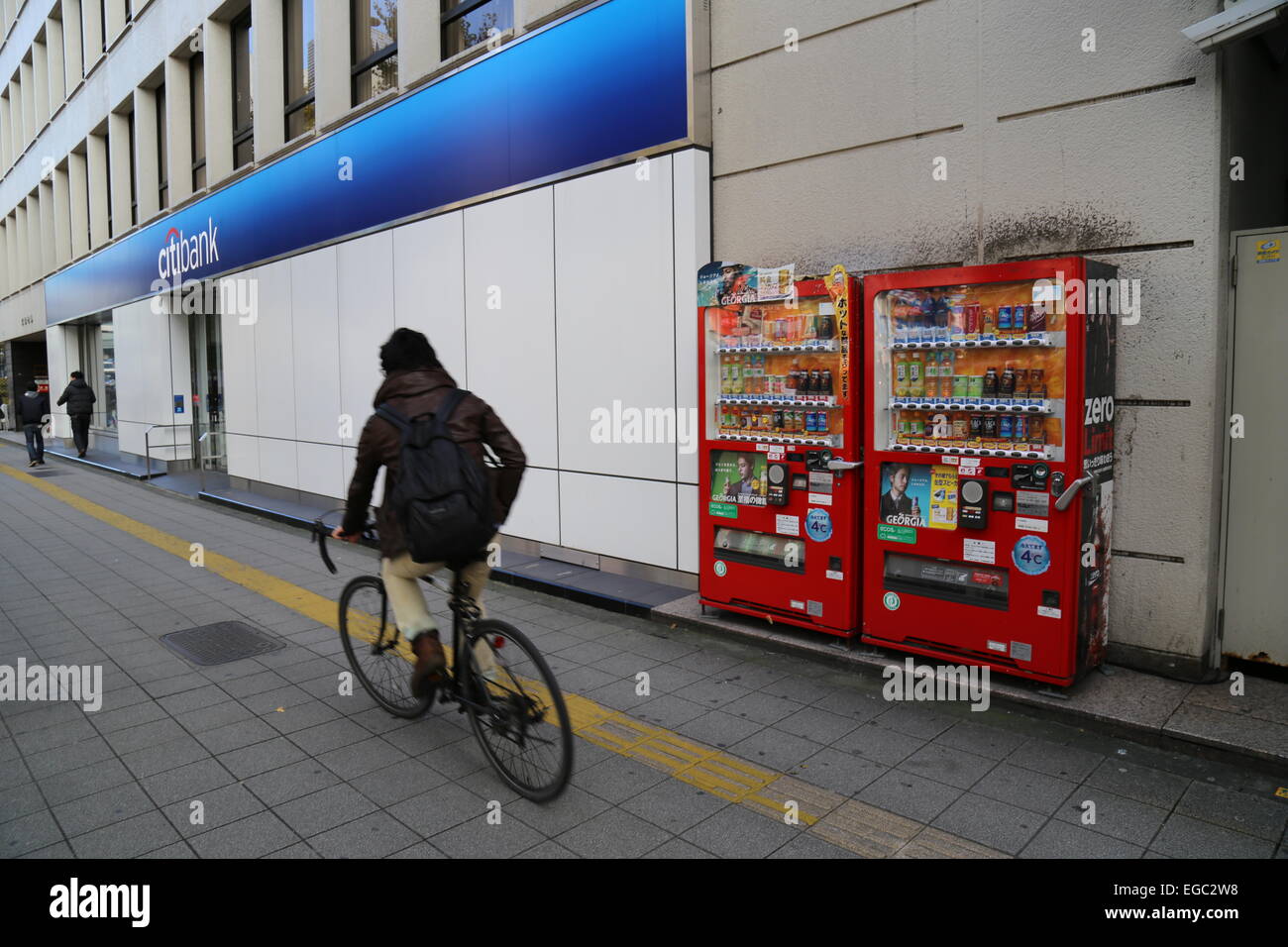 Un uomo in sella alla sua bicicletta passato due distributori automatici a Tokyo in Giappone. Foto Stock