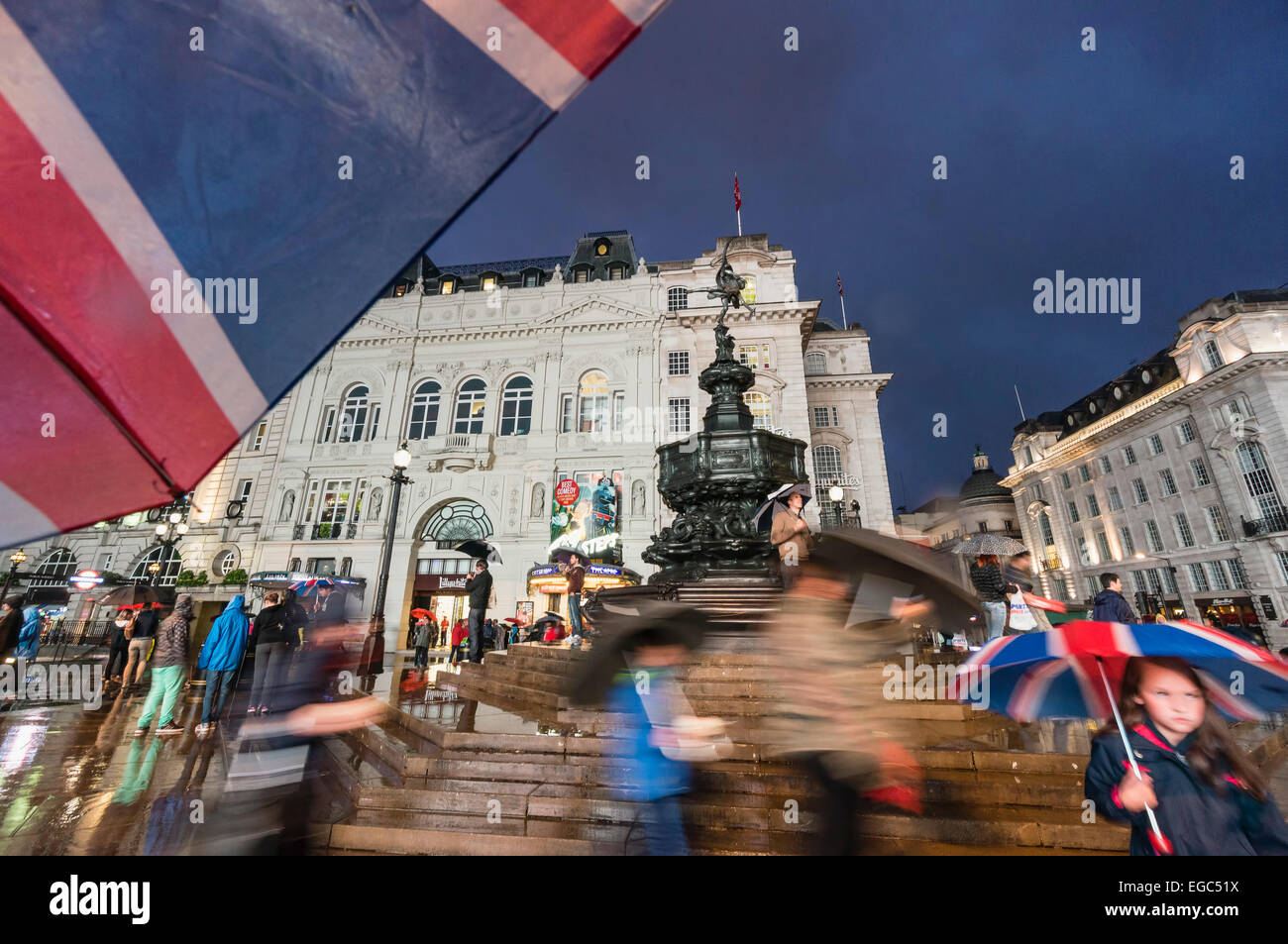 Persone con ombrelloni a Piccadilly Circus di notte, Londra, Regno Unito Foto Stock