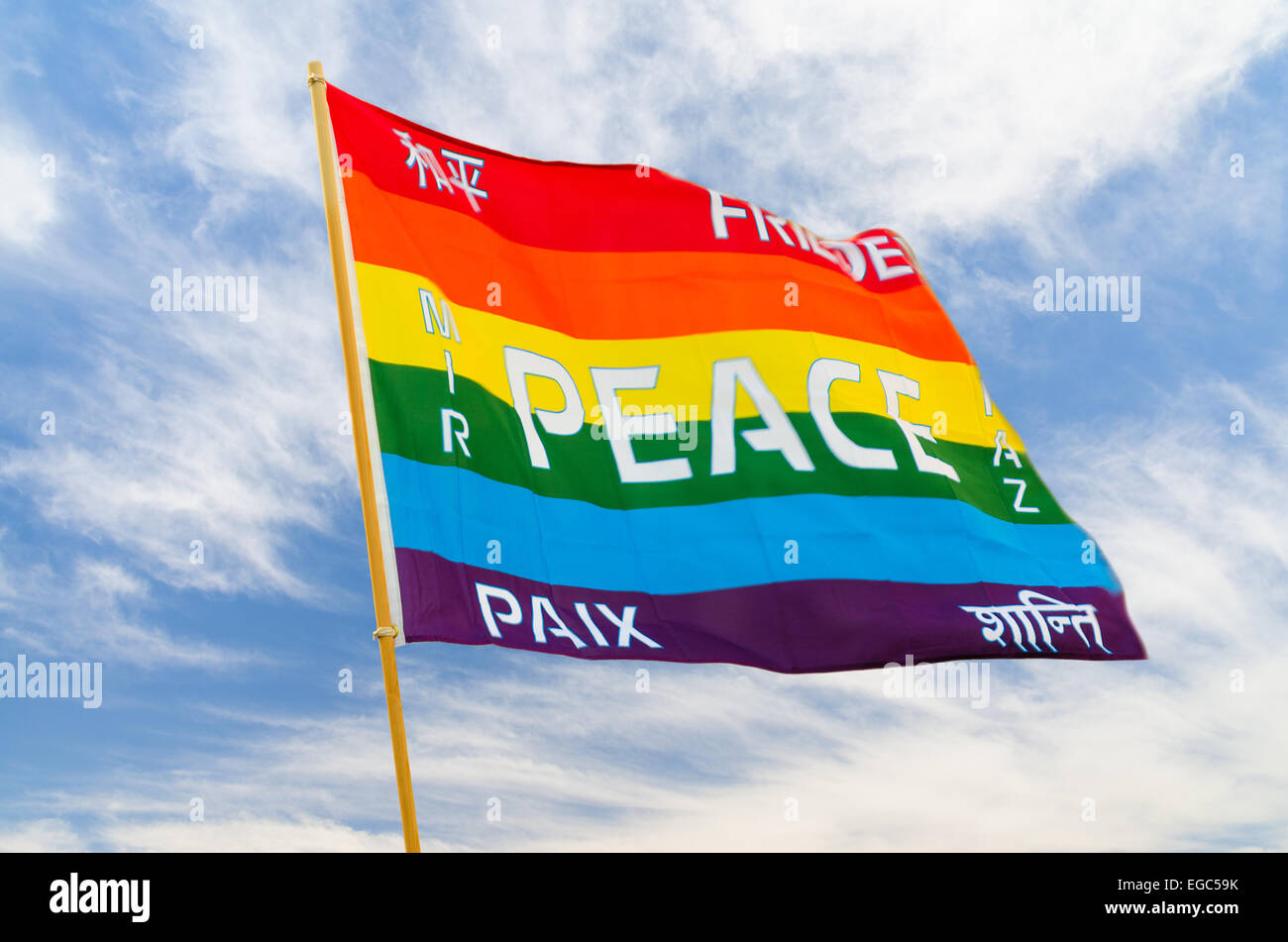 Sventolando rainbow varicolored bandiera della pace con multilingue testo pacifico battenti sul vento contro il cielo blu Foto Stock