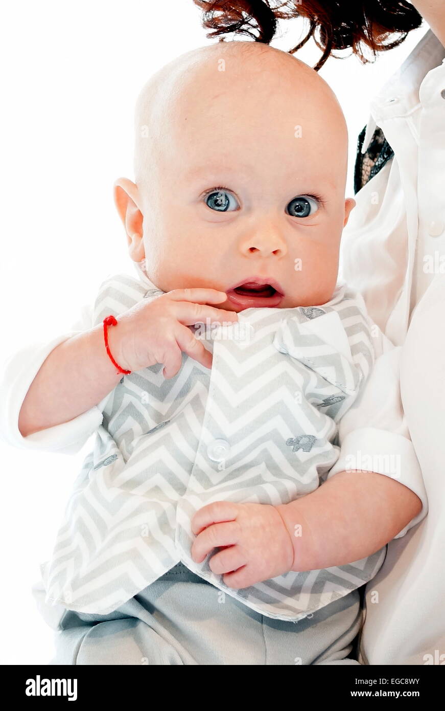 Bambino con occhi blu carino con filo rosso intorno al polso (kabbalah), mettendo la mano in bocca. Foto Stock