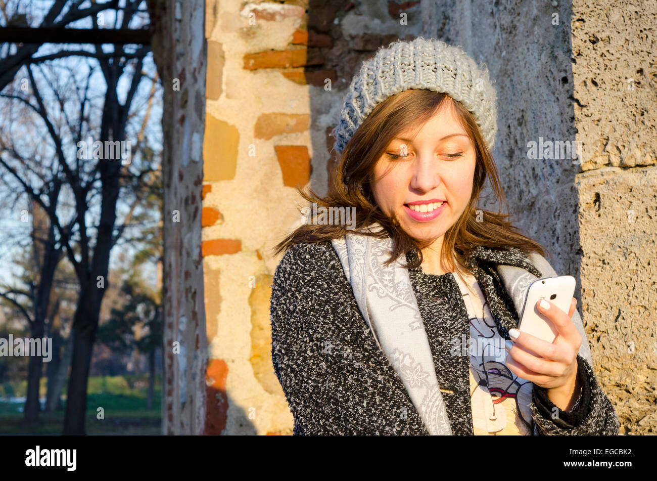 Ragazza sorridente la lettura di un messaggio sullo smartphone all'aperto in un parco Foto Stock