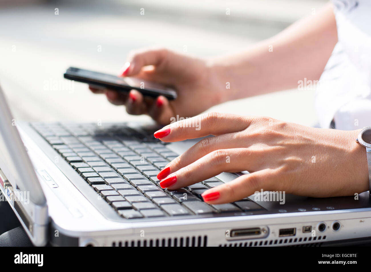 Le mani di una imprenditrice digitando su una tastiera di computer e tenendo il telefono in altro Foto Stock