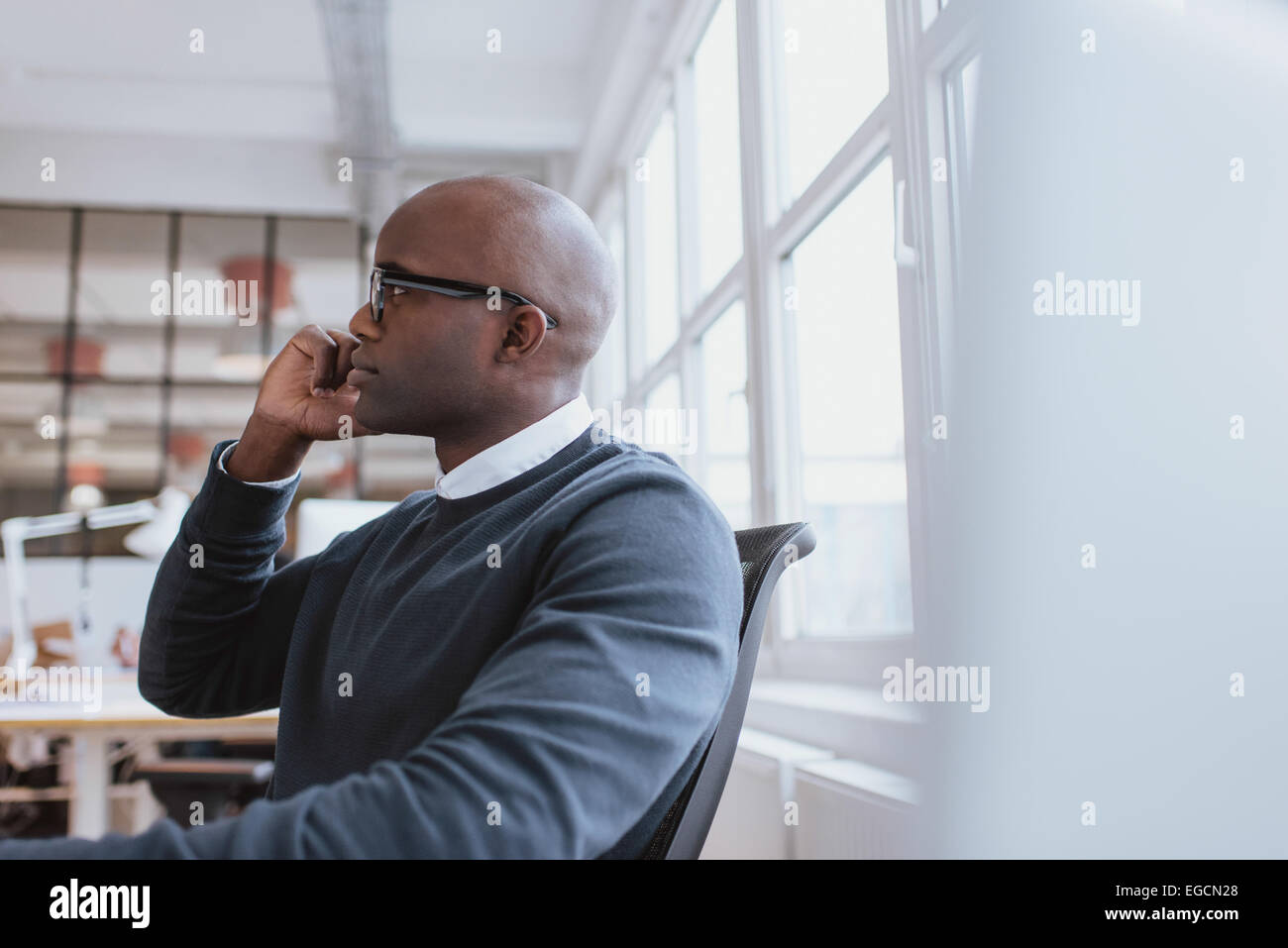 Vista laterale di African executive seduto alla sua scrivania utilizzando il telefono cellulare. Giovane uomo al lavoro rispondendo a una chiamata telefonica. Foto Stock