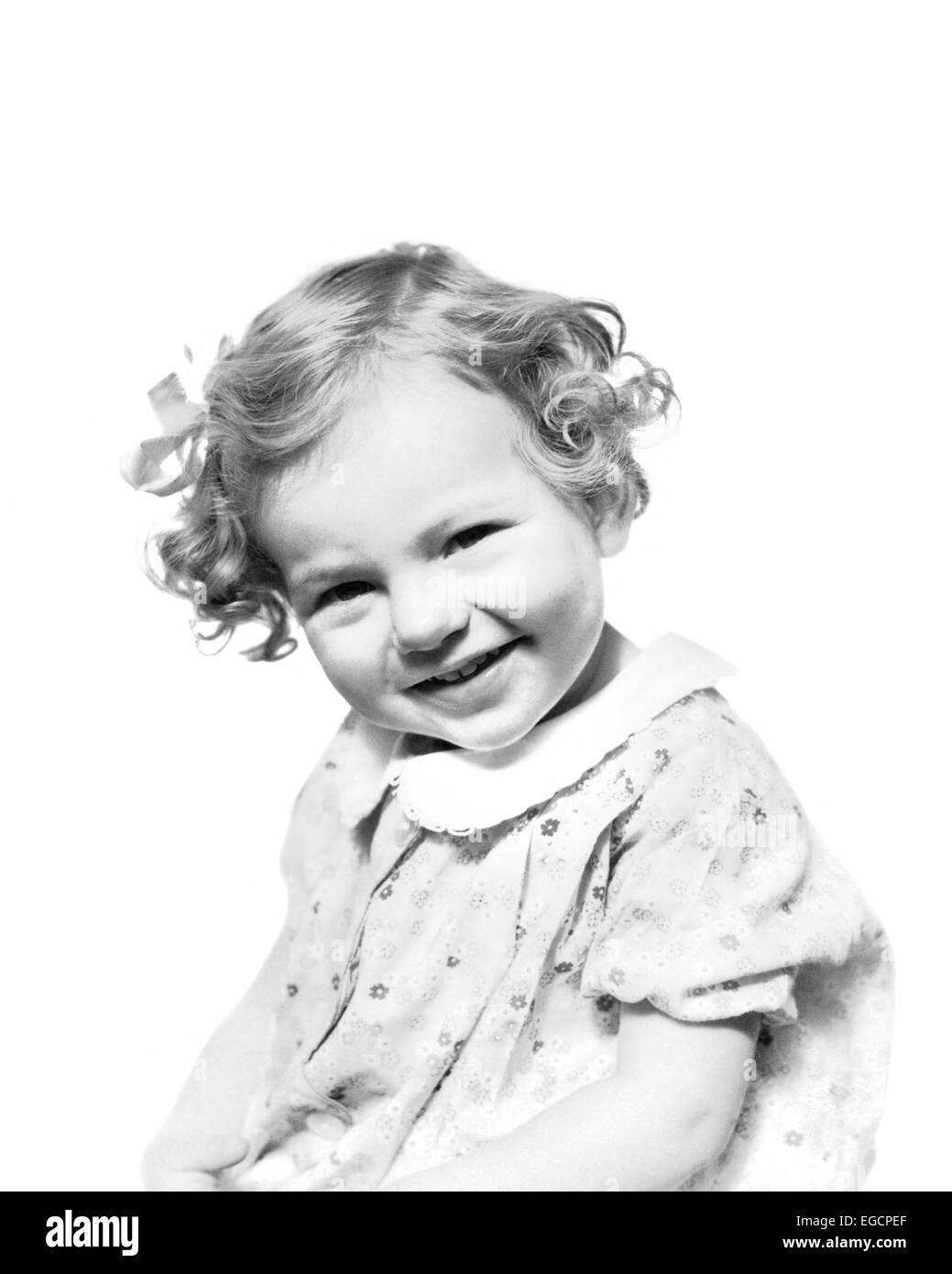 1930s sorridente ragazza TODDLER breve capelli ricci con arco indossando abiti stampa guardando la fotocamera Foto Stock