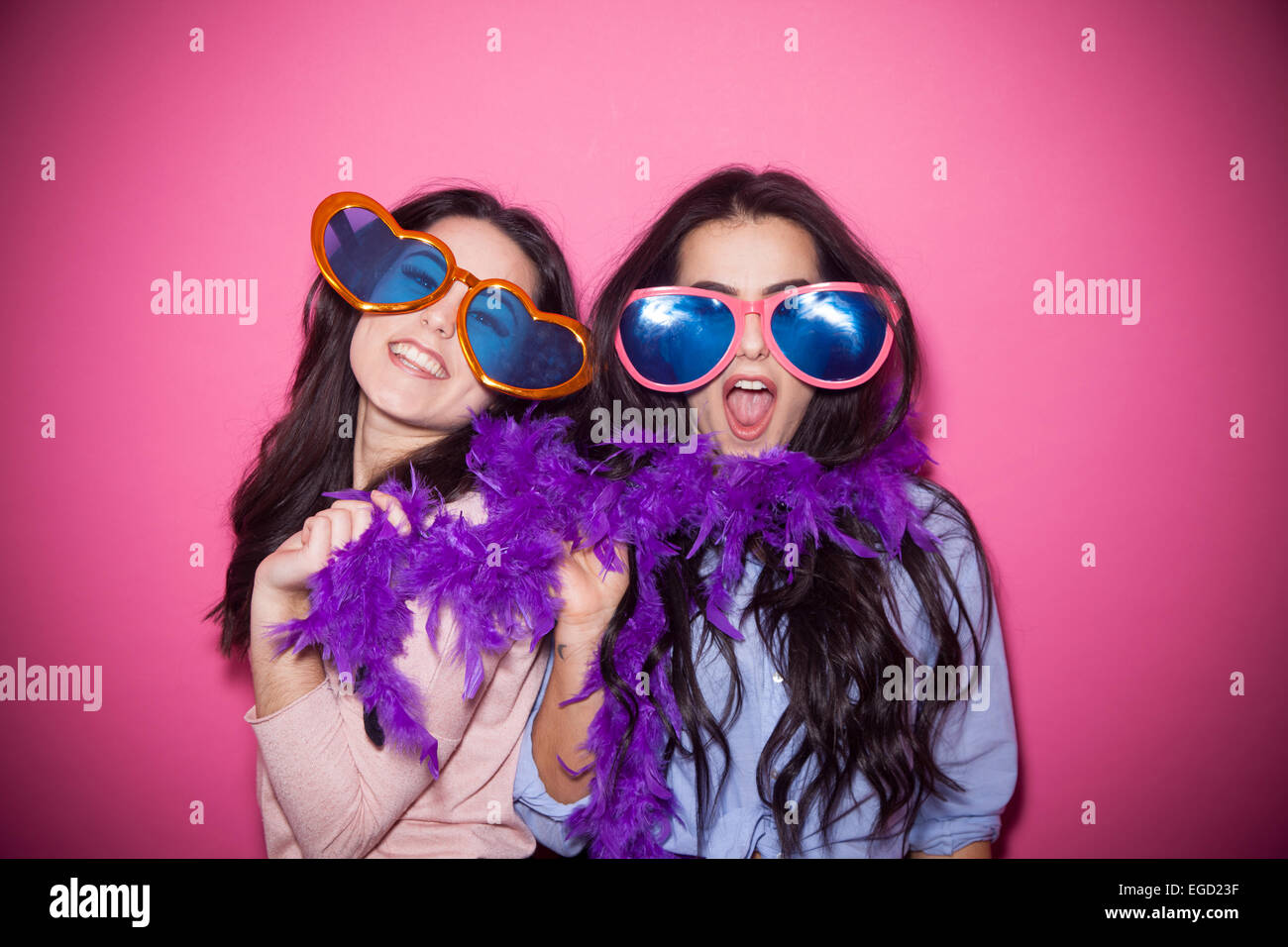 Due sorelle giocando con la commedia i bicchieri e una boa di piume. Foto Stock