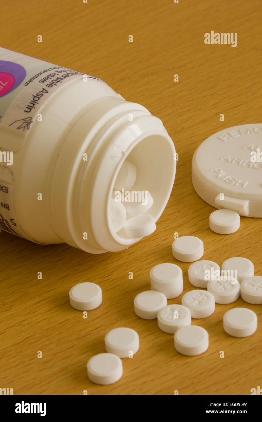 Bottiglia di aspirina sul suo lato con compresse versato su un tavolo Foto Stock
