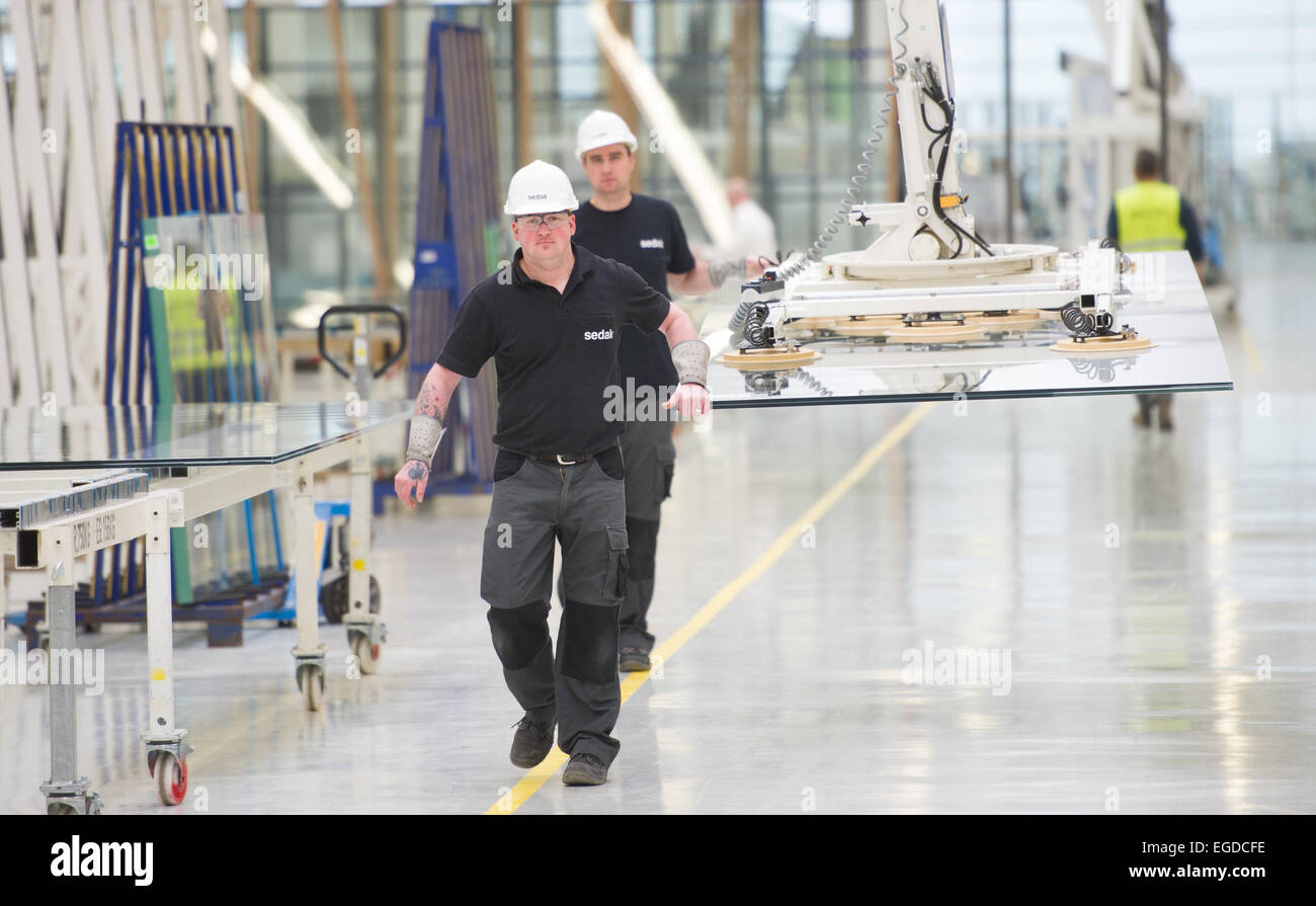 Gersthofen, Germania. Il 23 febbraio, 2015. Lavoratori in fabbrica trasportare una lastra di vetro con una gru che lo trattiene con ventose a Seele i fabbricanti di vetro Gersthofen, Germania, 23 febbraio 2015. Seele rende il vetro delle scale per tutti i negozi Apple Store di tutto il mondo e produce anche le lastre di vetro per le facciate del nuovo Apple Campus 2. Foto: Tobias Hase/dpa/Alamy Live News Foto Stock