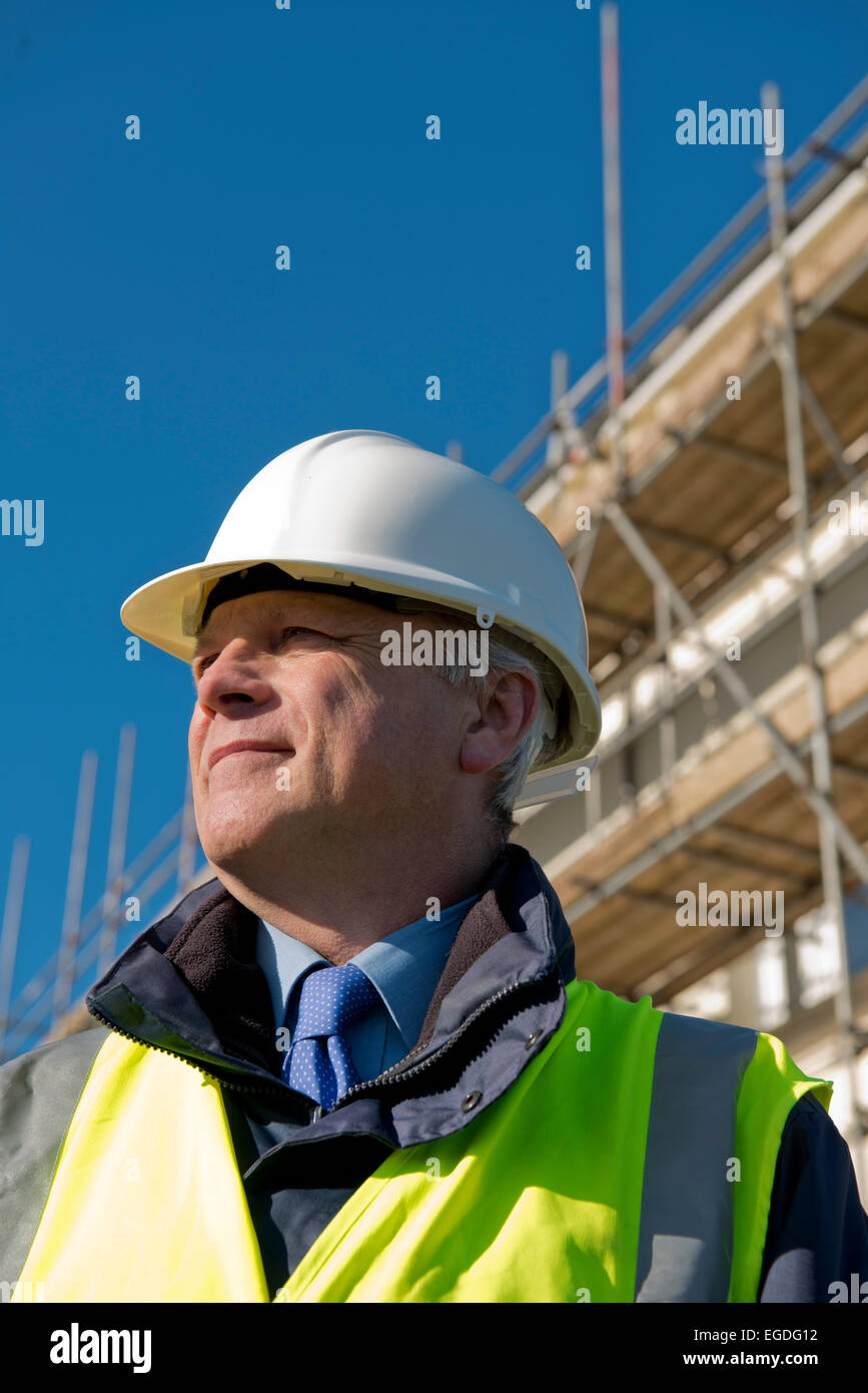 Basso angolo di visione verticale di un sorridente sito in costruzione foreman contro un cielo blu chiaro. Foto Stock