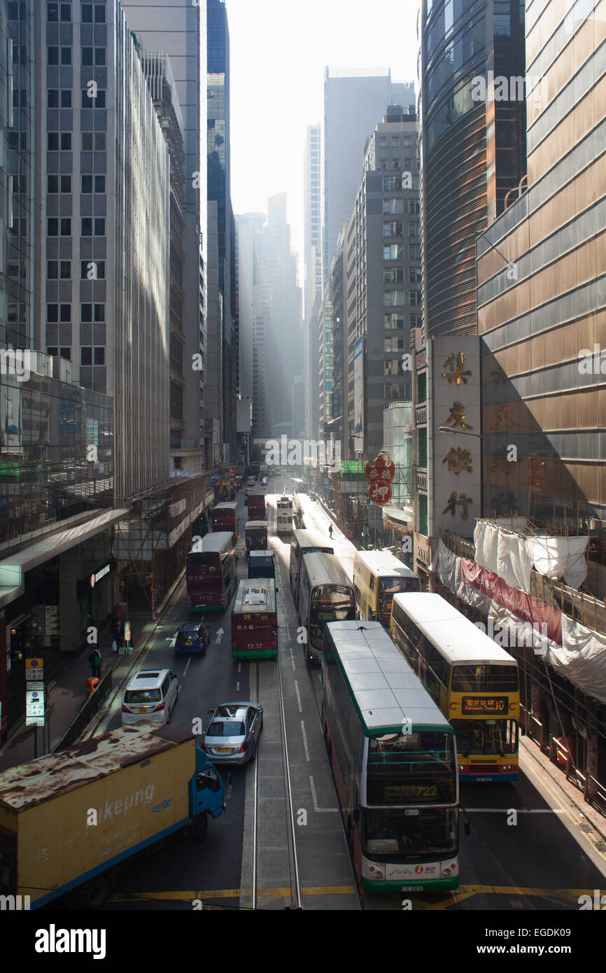 Des Voeux Road e il traffico nel sole di mattina nel distretto centrale. Gli autobus, i tram e le automobili porta le persone a lavorare presto la mattina. Foto Stock