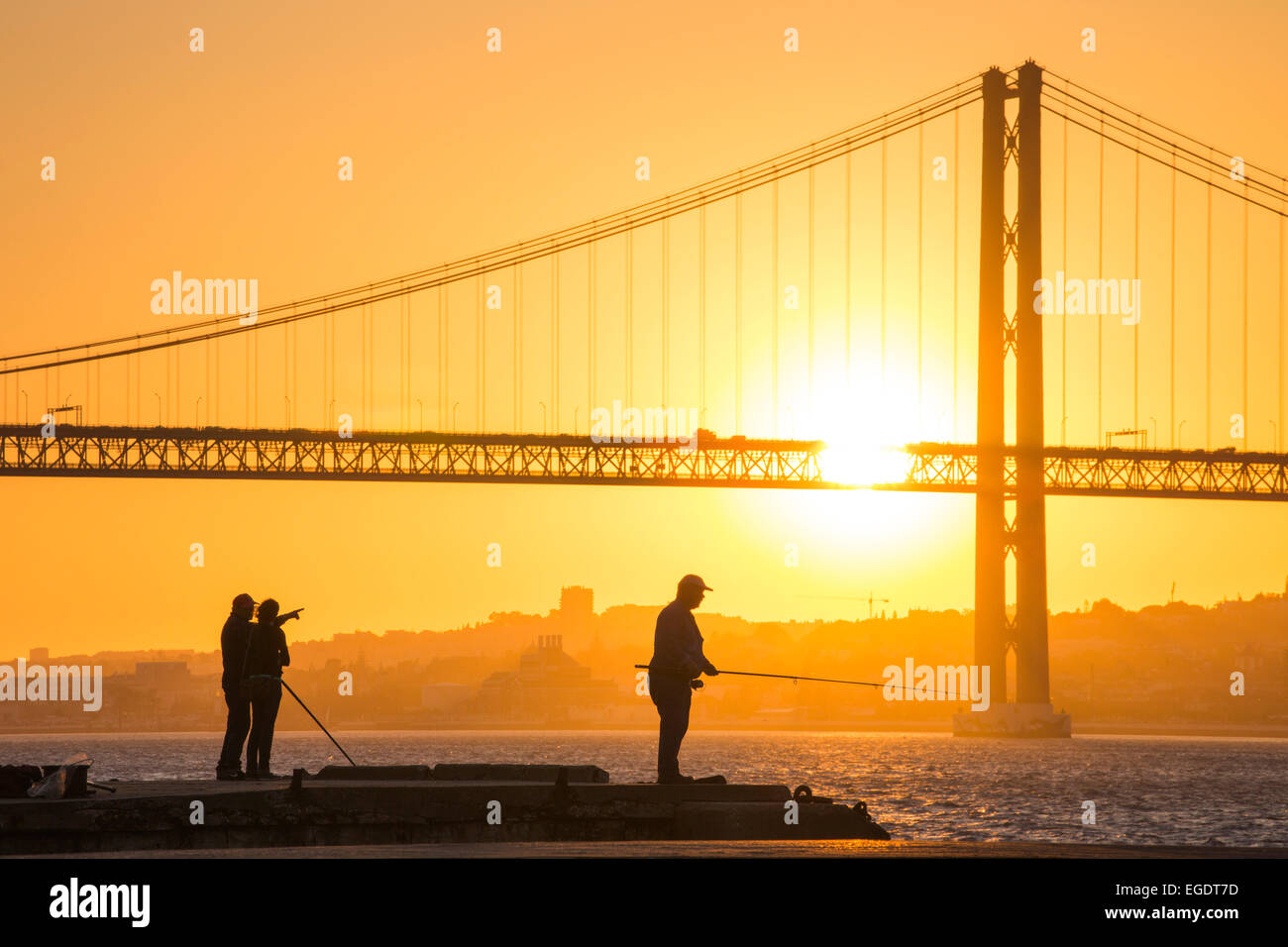 Silhouette di pescatori sul lungomare di Cacilhas con Ponte 25 de Abril ponte sul fiume Tago al tramonto, Cacilhas, Almada (vicino a Lisbona, Portogallo Foto Stock