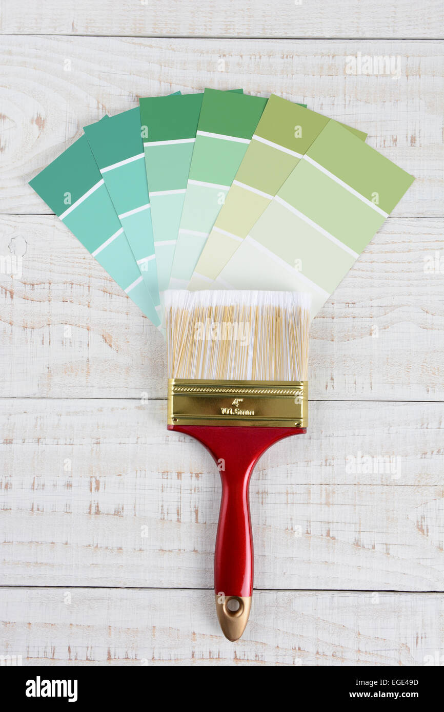 Overhead shot verticale di una spazzola di vernice e le sfumature di colore verde in campioni su un rustico in legno bianco superficie. Foto Stock
