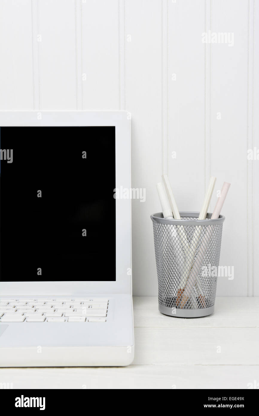 Primo piano di una casa bianca ufficio scrivania con computer portatile e Bicchiere portapenne. La scrivania di legno è di fronte a un bianco parete beadboard. L'immagine Foto Stock