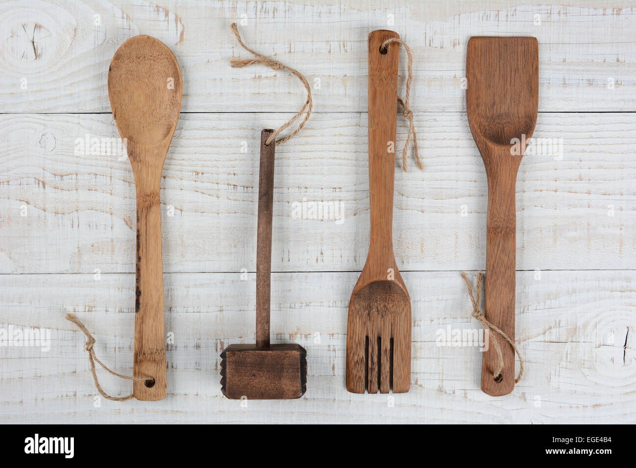 Angolo alto ingrandimento di un cucchiaio di legno, forcella e la spatola, mallet su un dipinto di bianco tavolo da cucina. Formato orizzontale. Foto Stock