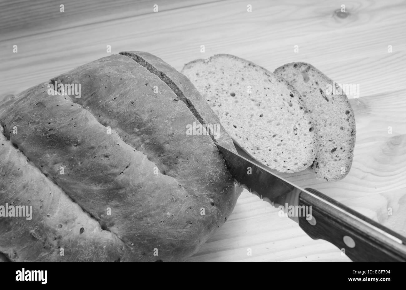 Il taglio delle fette di pane da una focaccia appena cotta su di un tavolo di legno - elaborazione monocromatica Foto Stock