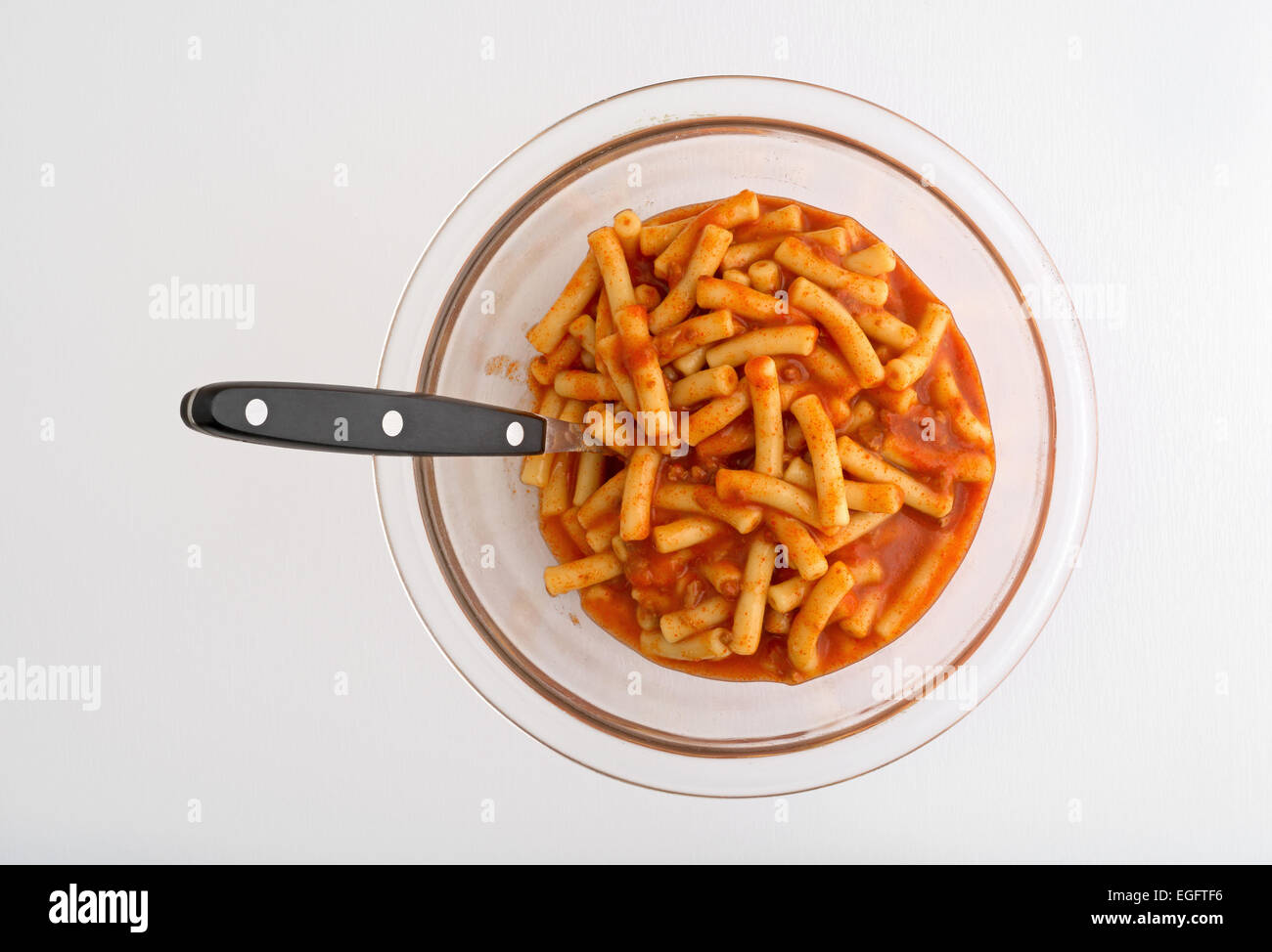 Semplice pasta in salsa di pomodoro farina in un recipiente di vetro con un manico nero cucchiaio sulla cima di un tavolo bianco con luce solare naturale da un vento Foto Stock