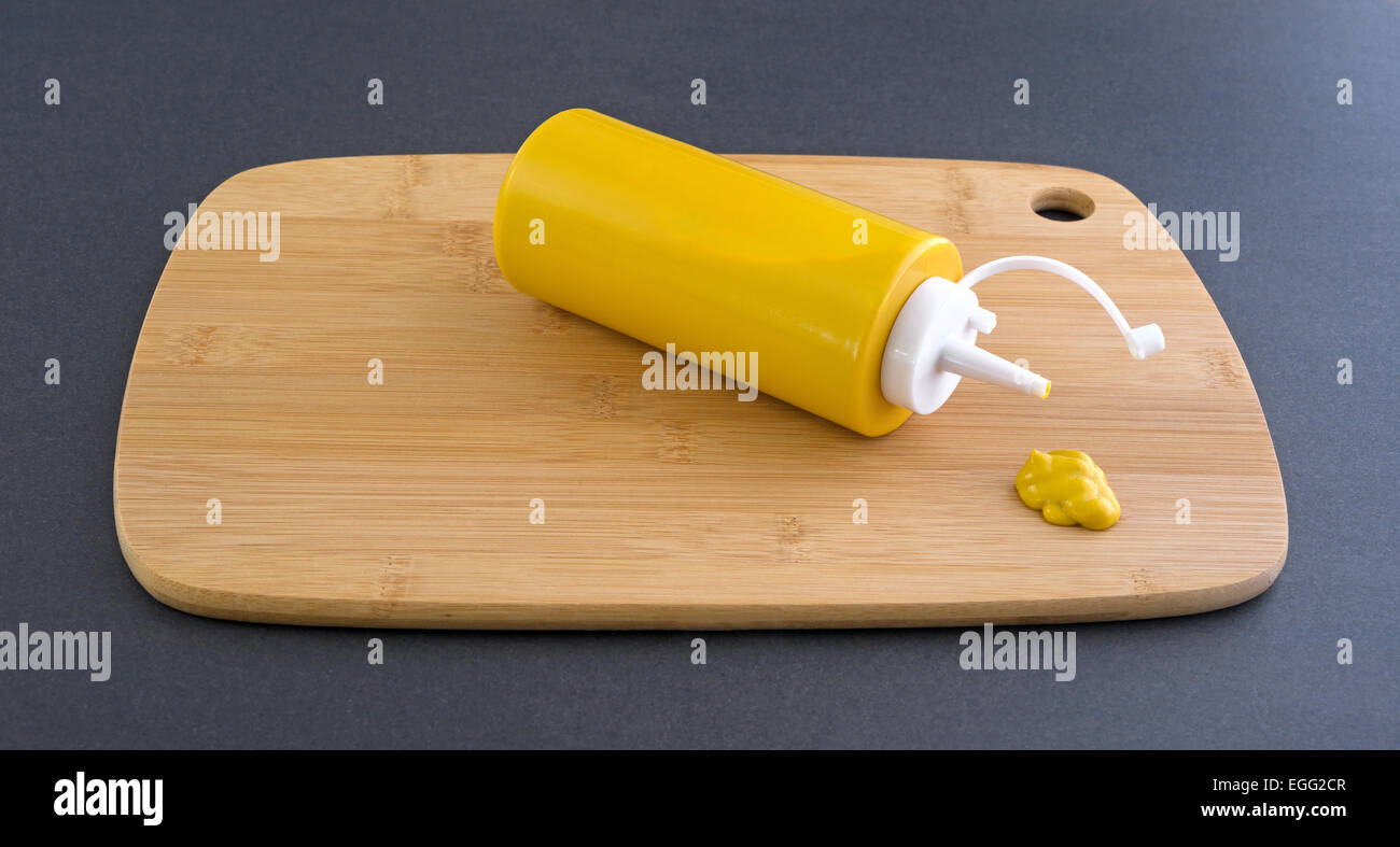 Una bottiglia di senape posa sul suo lato con un piccolo blob spremuto fuori di fronte su di un legno tagliere Foto Stock