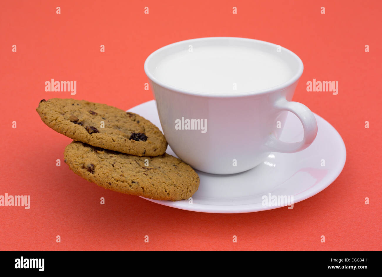 Due fiocchi d'avena raisin cookies su un piattino con latte intero in una tazza di caffè sulla cima di uno sfondo arancione Foto Stock