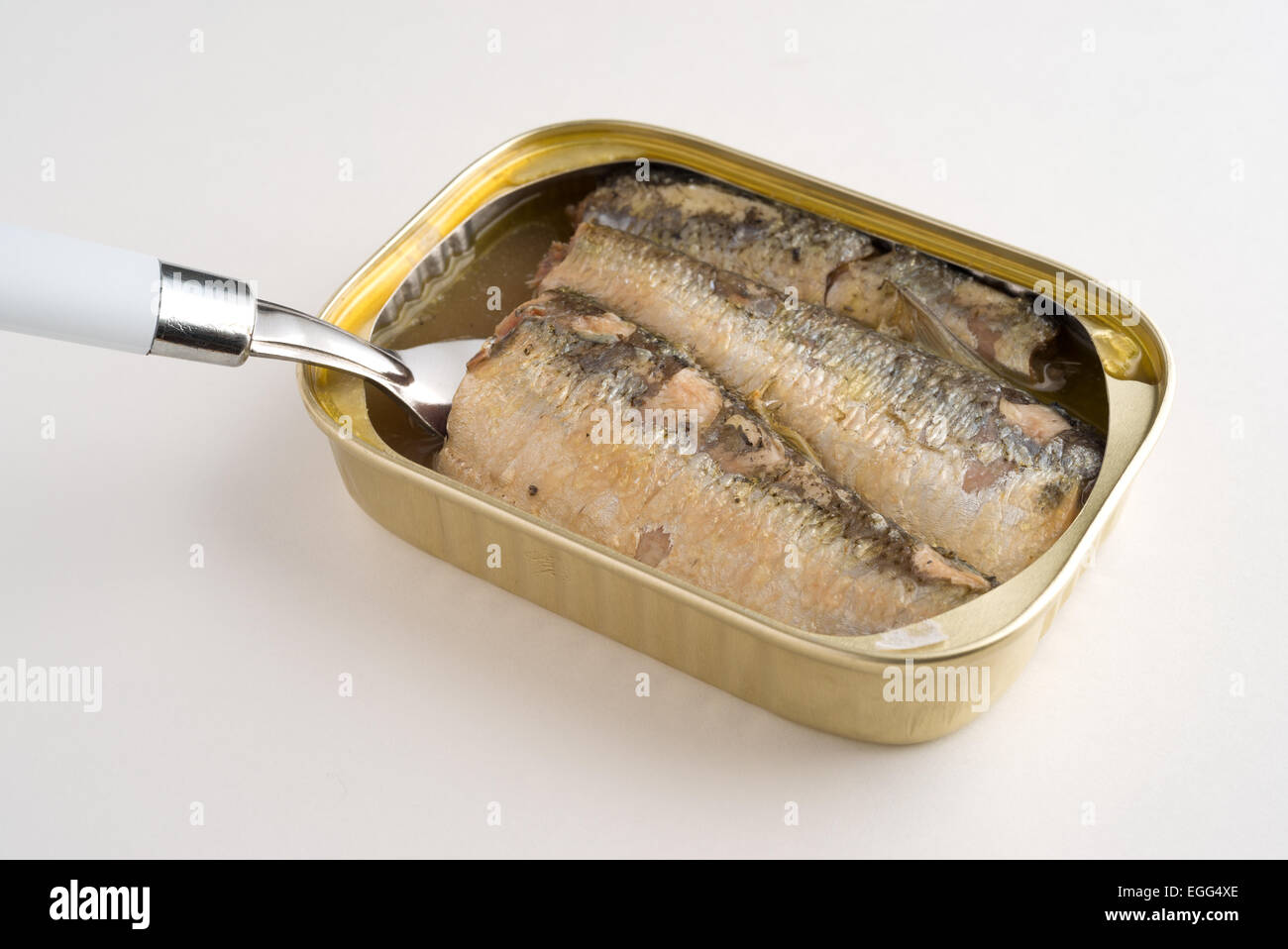 Un aperto può di sardine in olio e acqua con una forcella inserita nella teglia su un tavolo bianco alto. Foto Stock