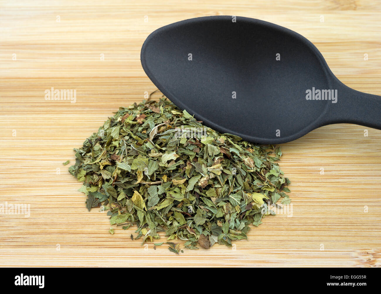 Una porzione di shredded menta verde erba foglie su un taglio di legno bordo nero con un cucchiaio. Foto Stock