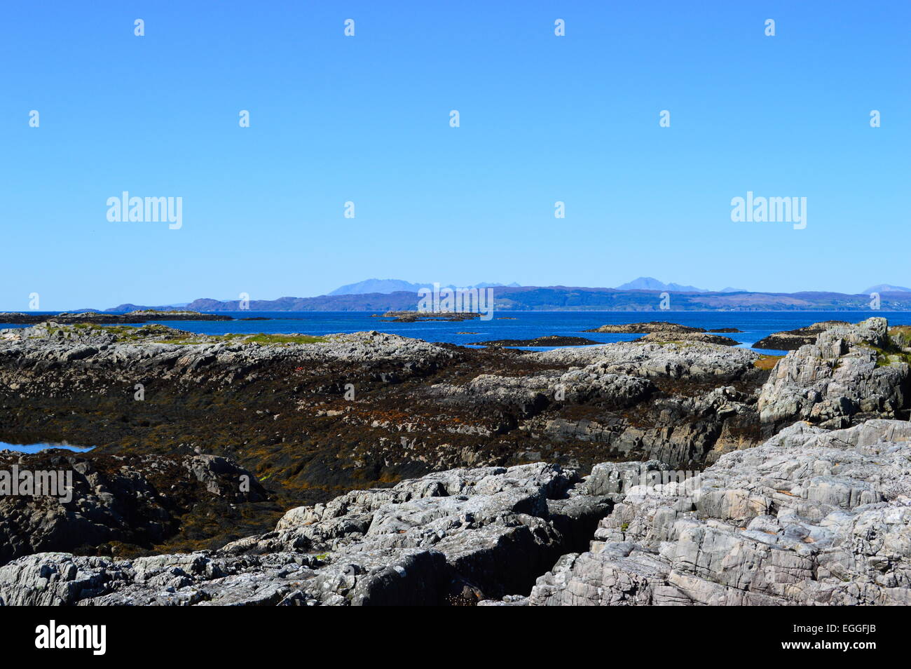 Spiaggia rocciosa vicino a Mallaig, Highlands Scozzesi. Skye e la Cuillins nella distanza, attraverso il suono di Sleat. Foto Stock