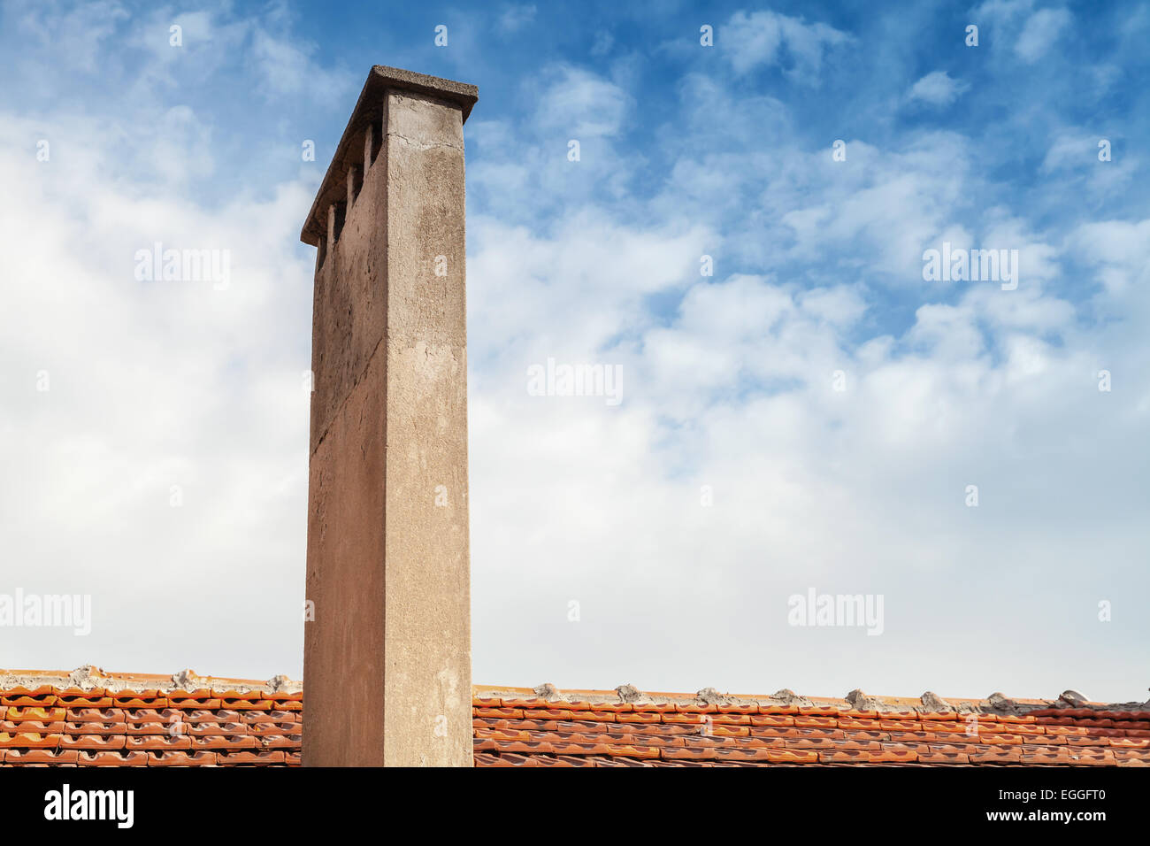 Grande ciminiera su rosso tetto di tegole con sfondo con cielo nuvoloso Foto Stock