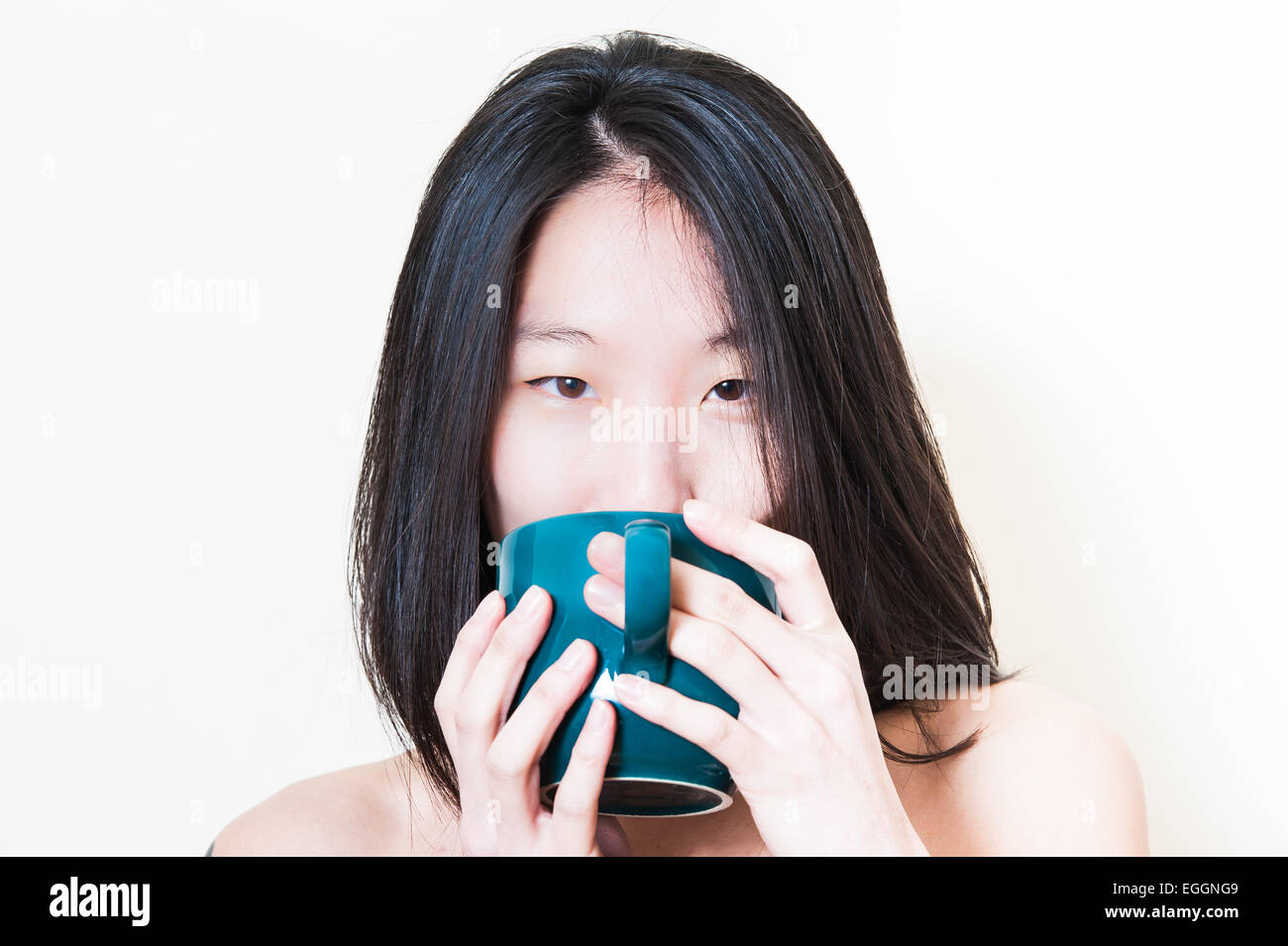 Giovane donna asiatica closeup mentre beve dal blu-verde tazza di petrolio su sfondo bianco Foto Stock