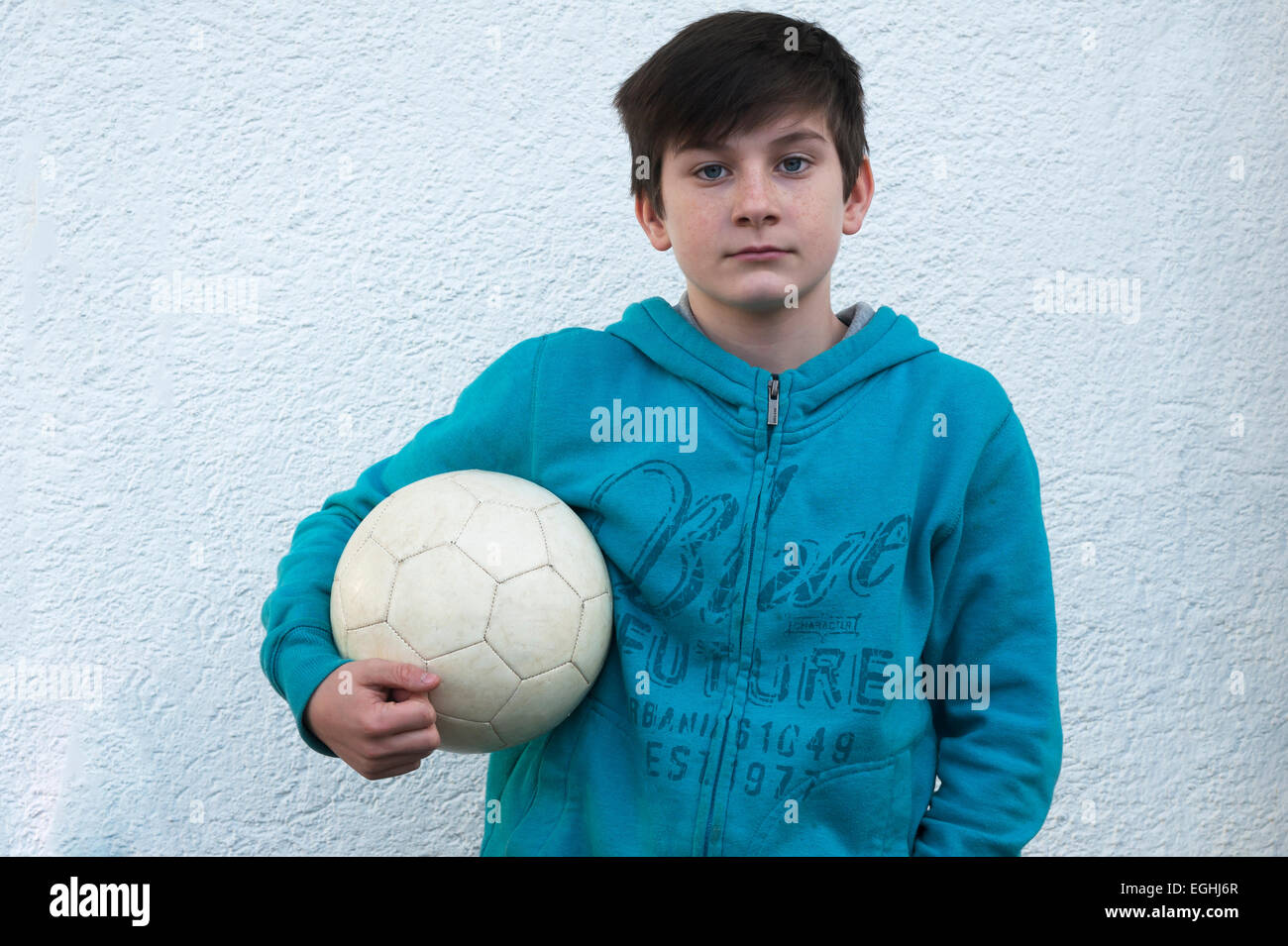 Il ragazzo, 10 anni, tenendo un calcio sotto il suo braccio, in piedi di fronte ad una parete bianca, Baden-Württemberg, Germania Foto Stock