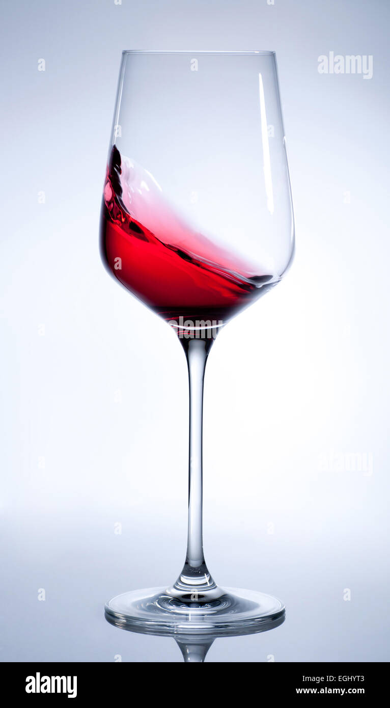 Vino rosso schizzi in elegante vetro su grigio Foto Stock