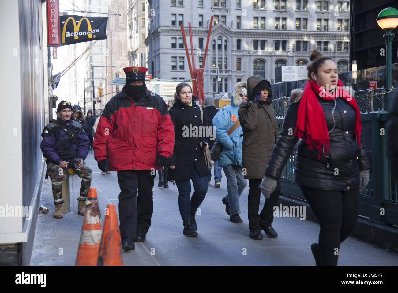 I pedoni a piedi lungo il Lower Broadway in condizioni di vento forte e temperature di congelamento in New York City. Foto Stock