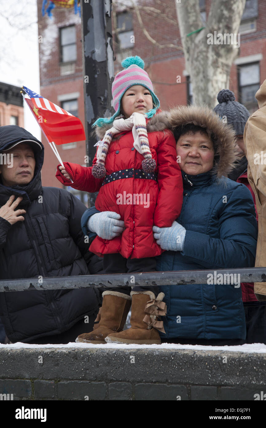 Bambino azienda cinese e bandierine americane con i nonni del quartiere Chinatown guardare la cerimonia petardo su chi Foto Stock