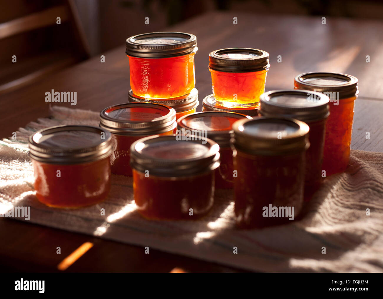 Appena fatta Siviglia marmellata di arance è retro-illuminato da un early morning sun. Il conservare i vasetti sono seduti su un tavolo di legno. Foto Stock
