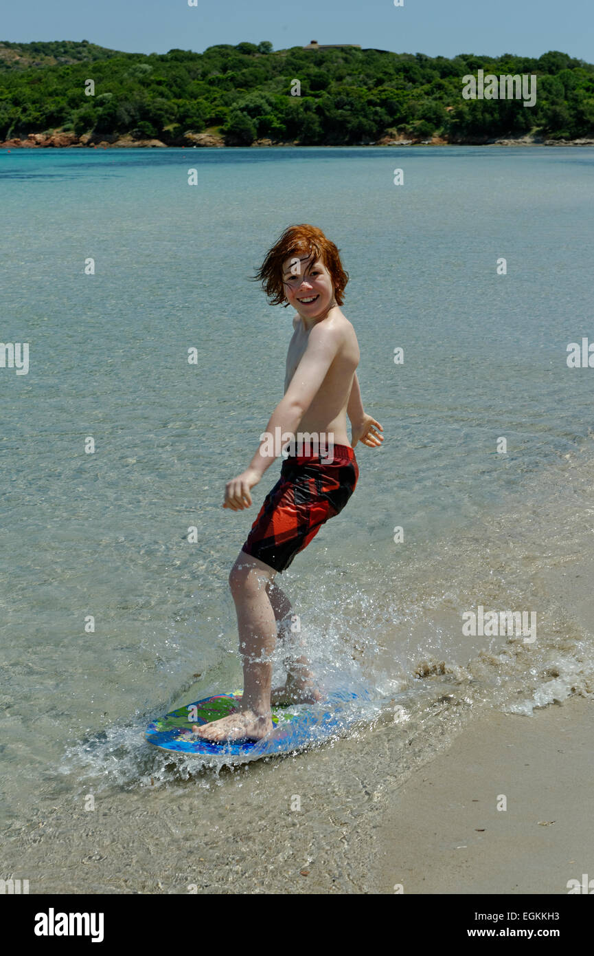 Ragazzo il surf con il suo boogie board, scheda di spiaggia o skimboard sulla spiaggia della baia di Rondinara, costa sudorientale, Corsica, Francia Foto Stock