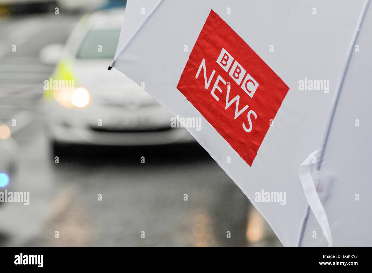 Ballyclare, Irlanda del Nord. 11 Settembre 2013 - Giornalista detiene una BBC News ombrello durante la visione di un'attività di polizia Foto Stock