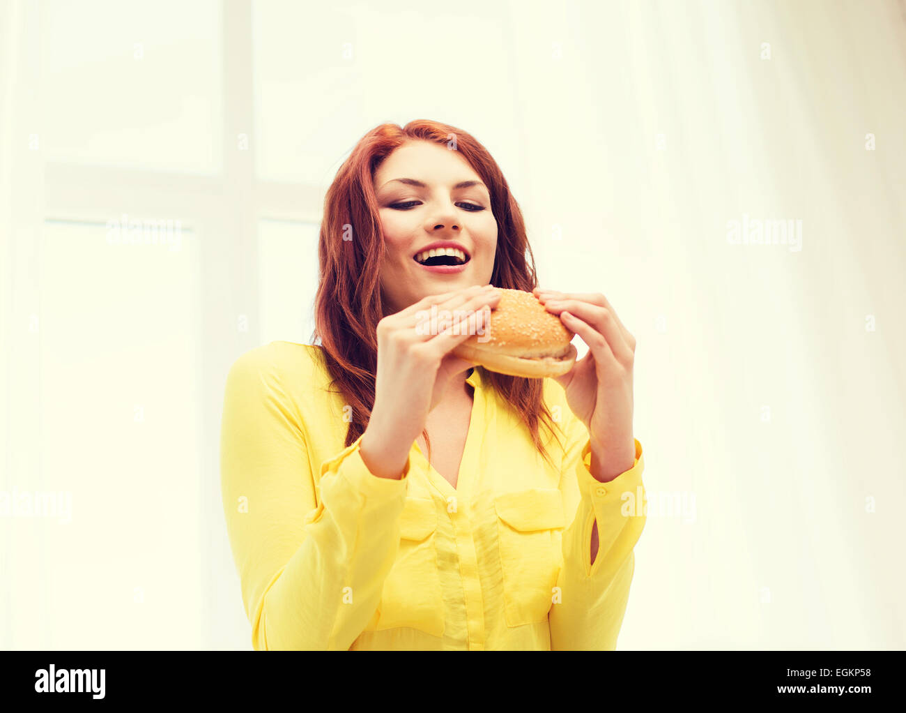 Sorridente giovane donna mangiare hamburger a casa Foto Stock