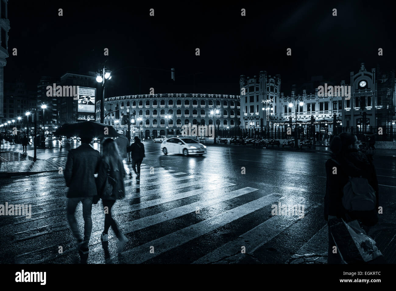 Le persone sotto gli ombrelloni su una notte piovosa sulle strade di Valencia in Spagna su un attraversamento pedonale Foto Stock