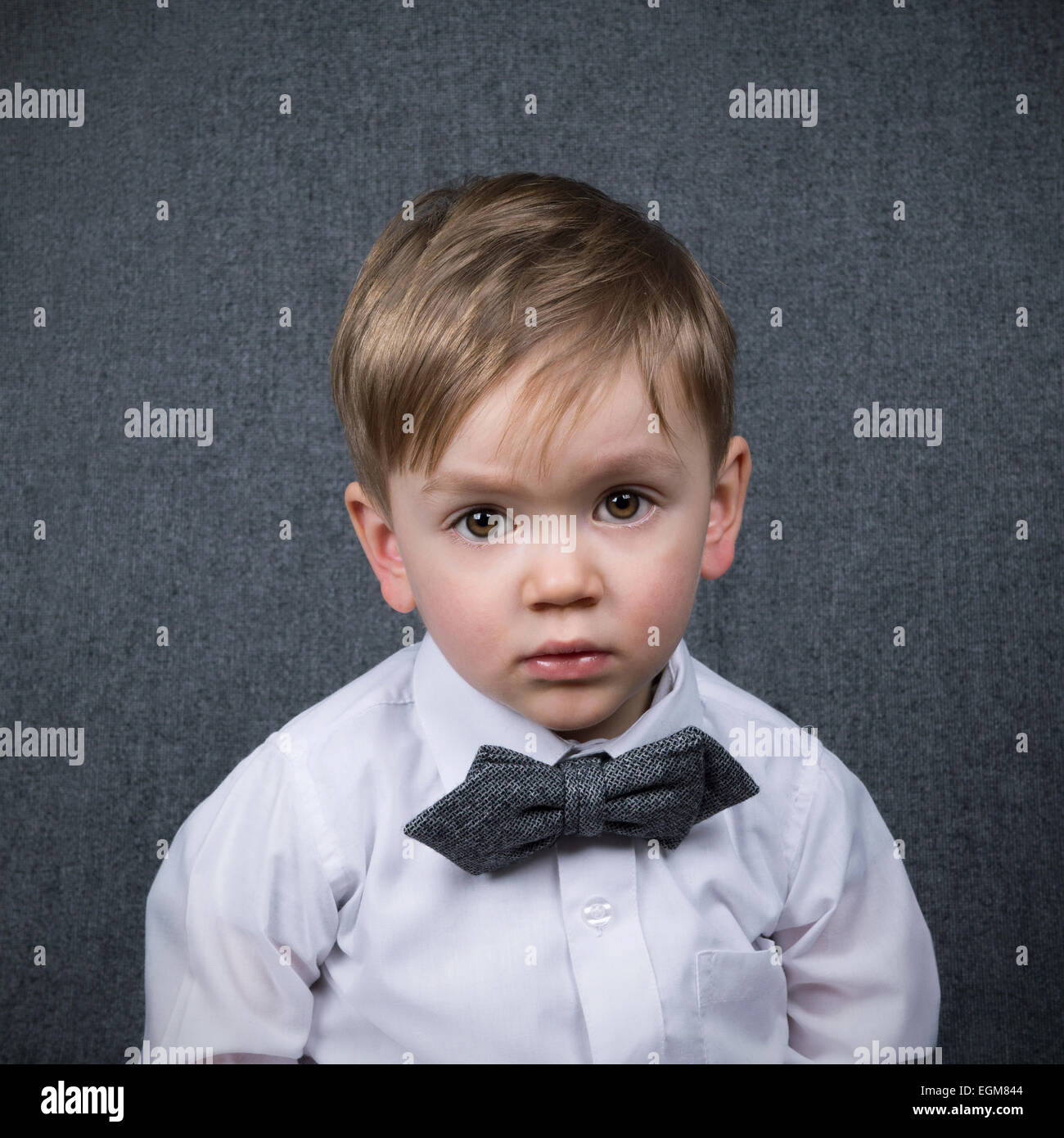 Due anni di vecchio ragazzo guardando dritto verso la fotocamera che indossa una cravatta a farfalla grigio Foto Stock